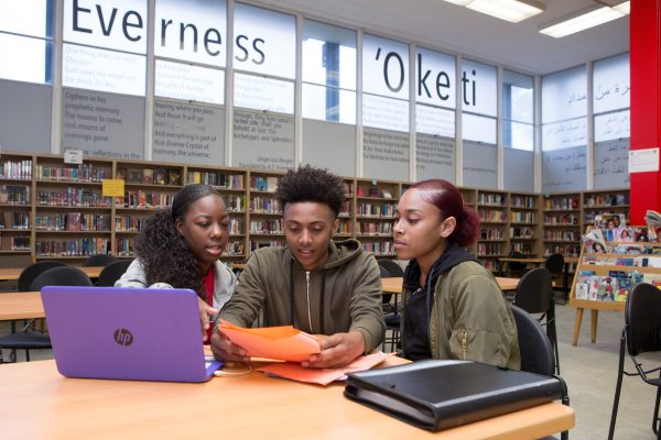 Two high school girls and a high school boy at a computer in the library.