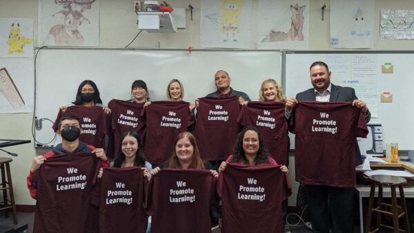 Students, teachers and school leaders holding up "We Promote Learning" t-shirts.